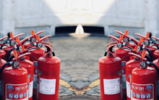 Conjuntos de extintores de polvo ABC de color rojo en el suelo frente a una caja de color rojo, ideales para combatir fuegos de clase A, B y C en espacios pequeños.